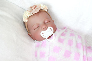A baby doll with a pacifier lies on a bed, highlighting its charming design and the peaceful setting.